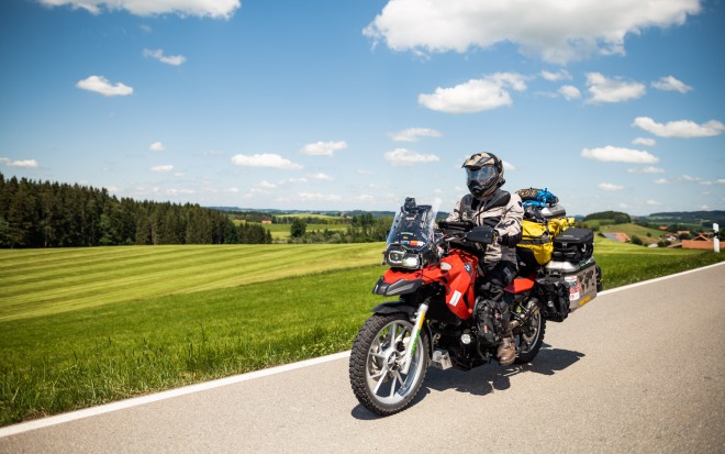 A motorcycle with dguard rides fully loaded on a road